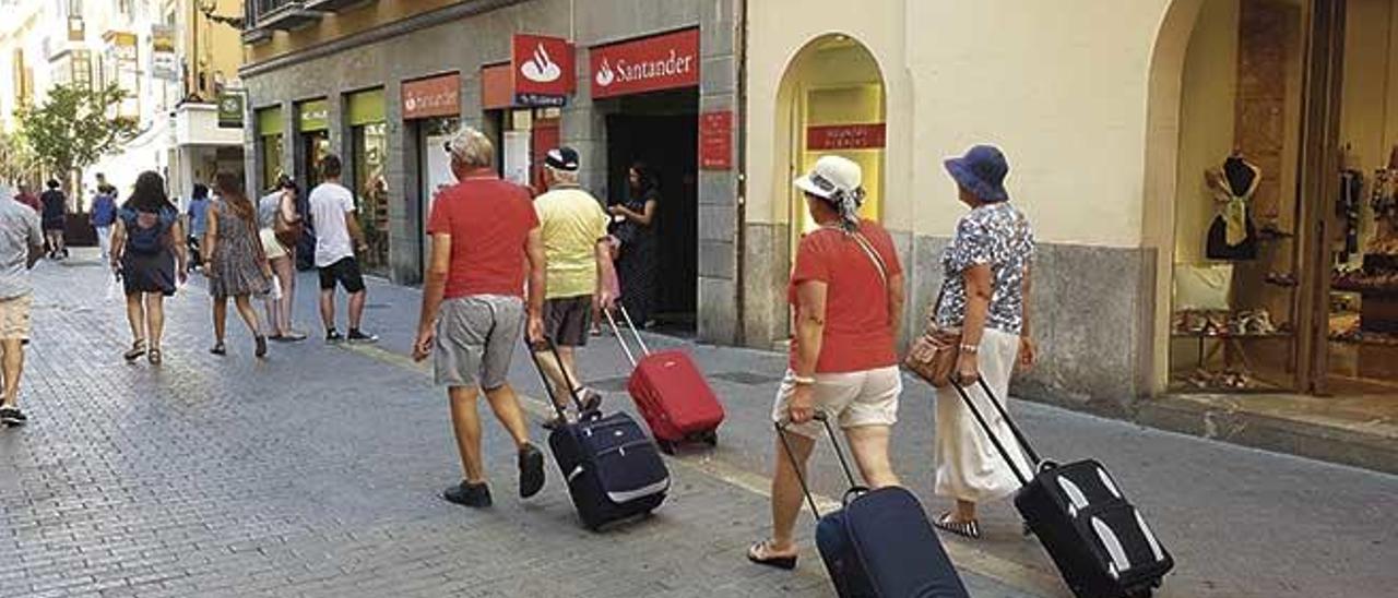 Varios turistas cruzan con sus maletas la peatonal calle Sant Miquel.