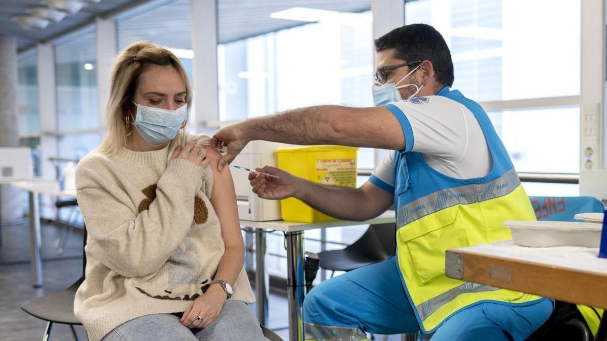 Un sanitario vacuna a una joven contra el COVID.