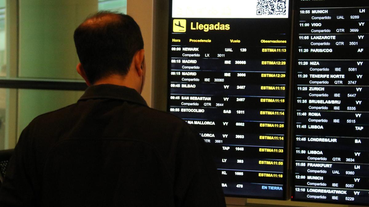 Un usuari mirant els taulells informatius a l'aeroport del Prat amb els vols afectats pel tancament de l'espai aeri.
