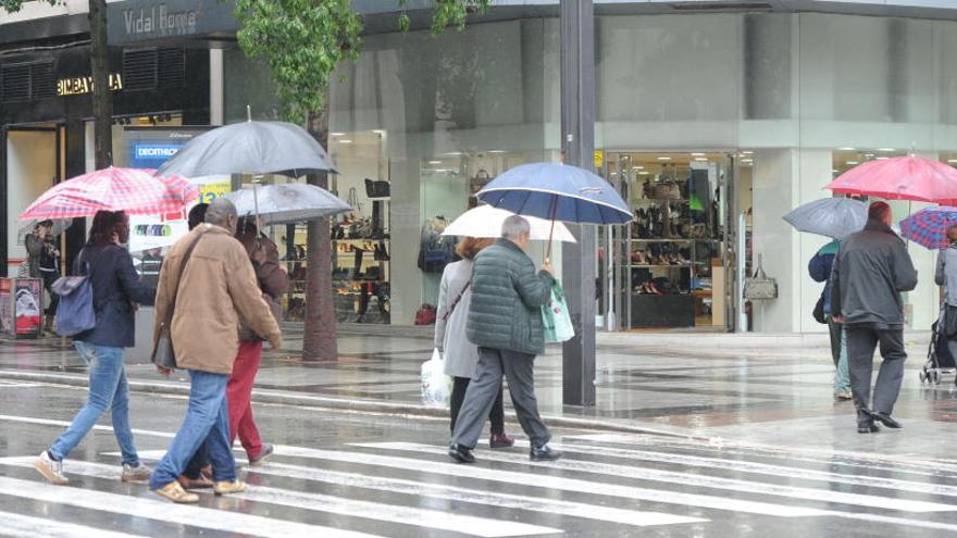 Personas con paraguas cruzan un paso de cebra bajo la lluvia.