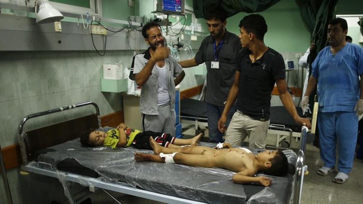 Un palestino llora junto a dos niños heridos en el bombardeo israelí contra el colegio de la ONU, este jueves.