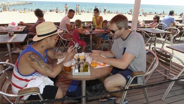 Dos turistas utilizan el móvil en una playa de Barcelona.