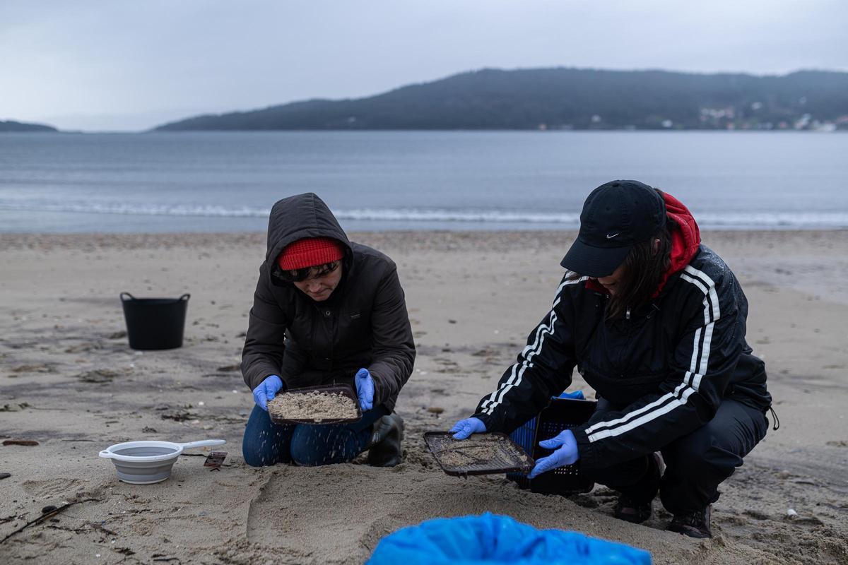 Dos personas limpiando una playa tras el vertido de pélets del Toconao