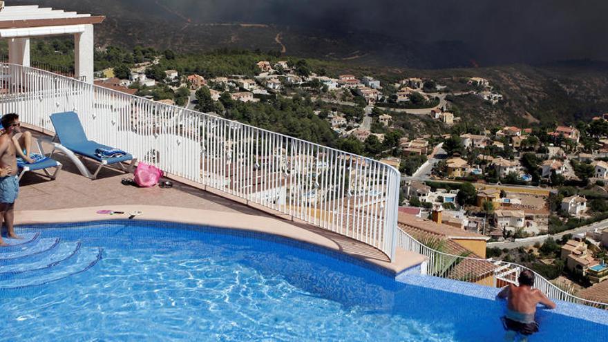 Dos vecinos de una urbanización de Benitatxell observan las llamas desde su piscina.