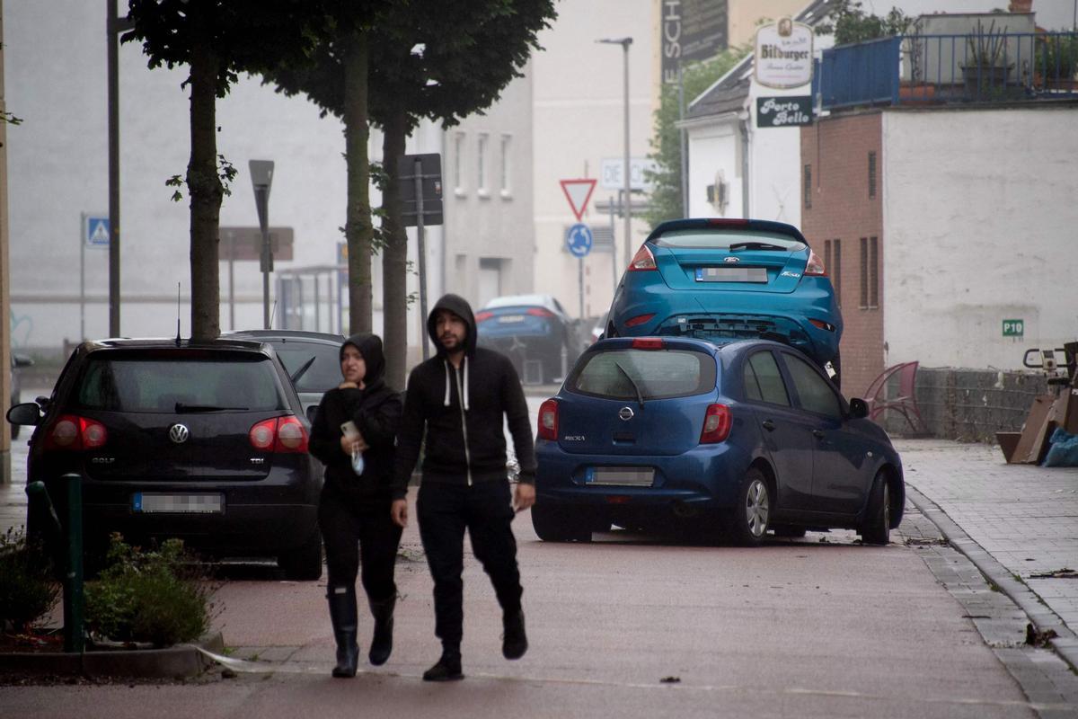 Dos personas pasan junto a coches dañados tras las fuertes lluvias en Euskirchen, en el oeste de Alemania.