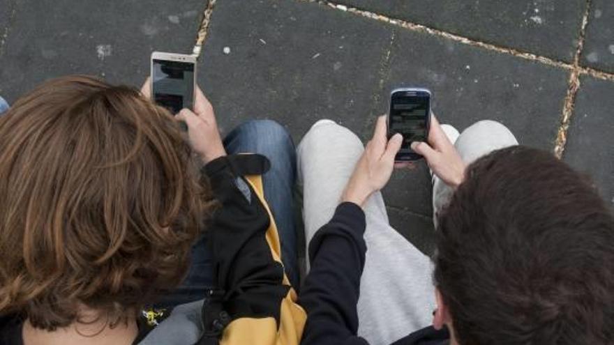 Dos adolescentes utilizando el teléfono móvil en la calle.