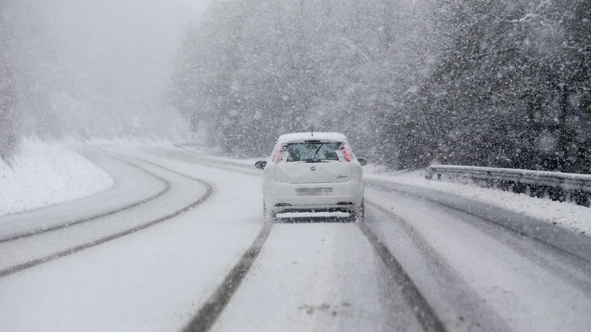 Un coche circulando por el medio de una carretera nevada
