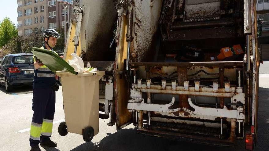 Un operario de recogida de basura mete en el camión un contenedor verde.