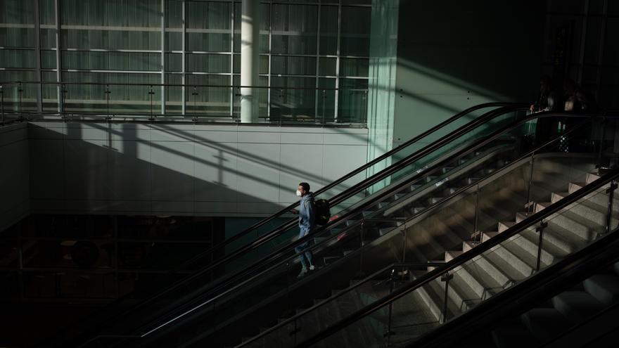 Un home amb una maleta en les escales mecàniques de l'Aeroport del Prat, a Barcelona