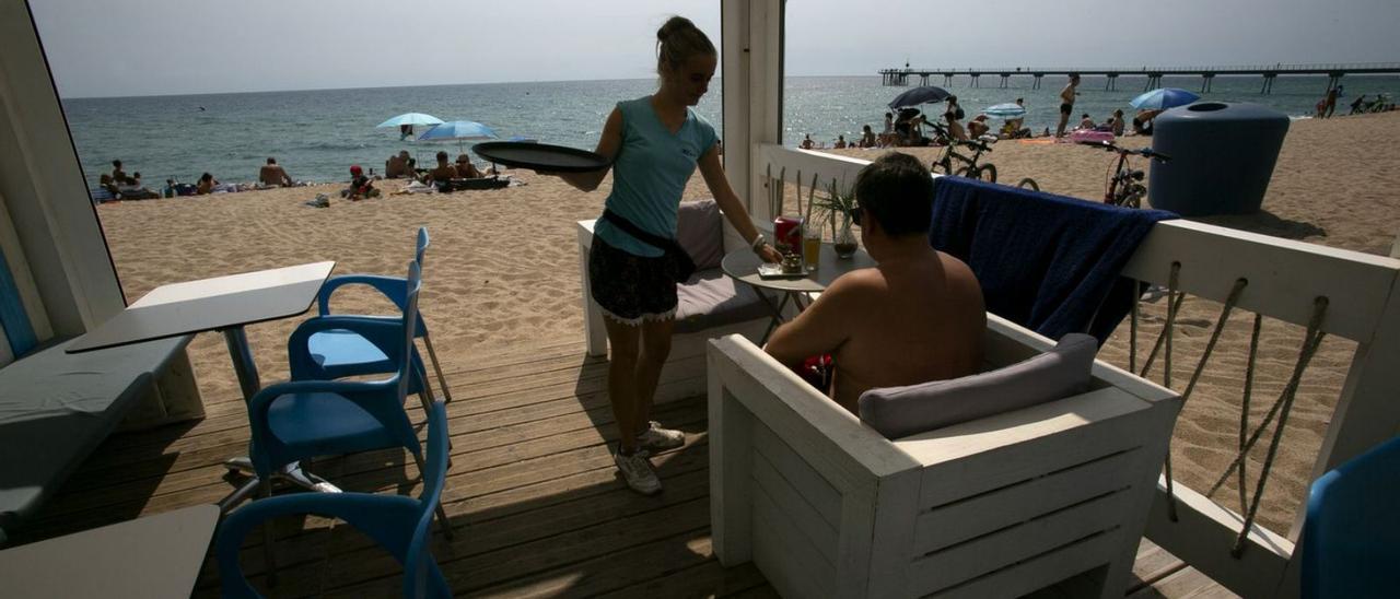 Una cambrera serveix una consumició a un client en un establiment de platja. | DIARI DE GIRONA