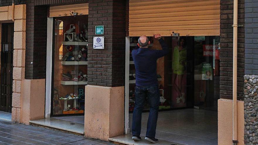 Un comerciante del barrio valenciano de Benimaclet echa la persiana de su negocio.