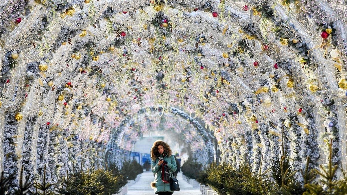 Una joven pasea bajo un túnel de luces navideñas, bajo el frío de Moscú en diciembre.