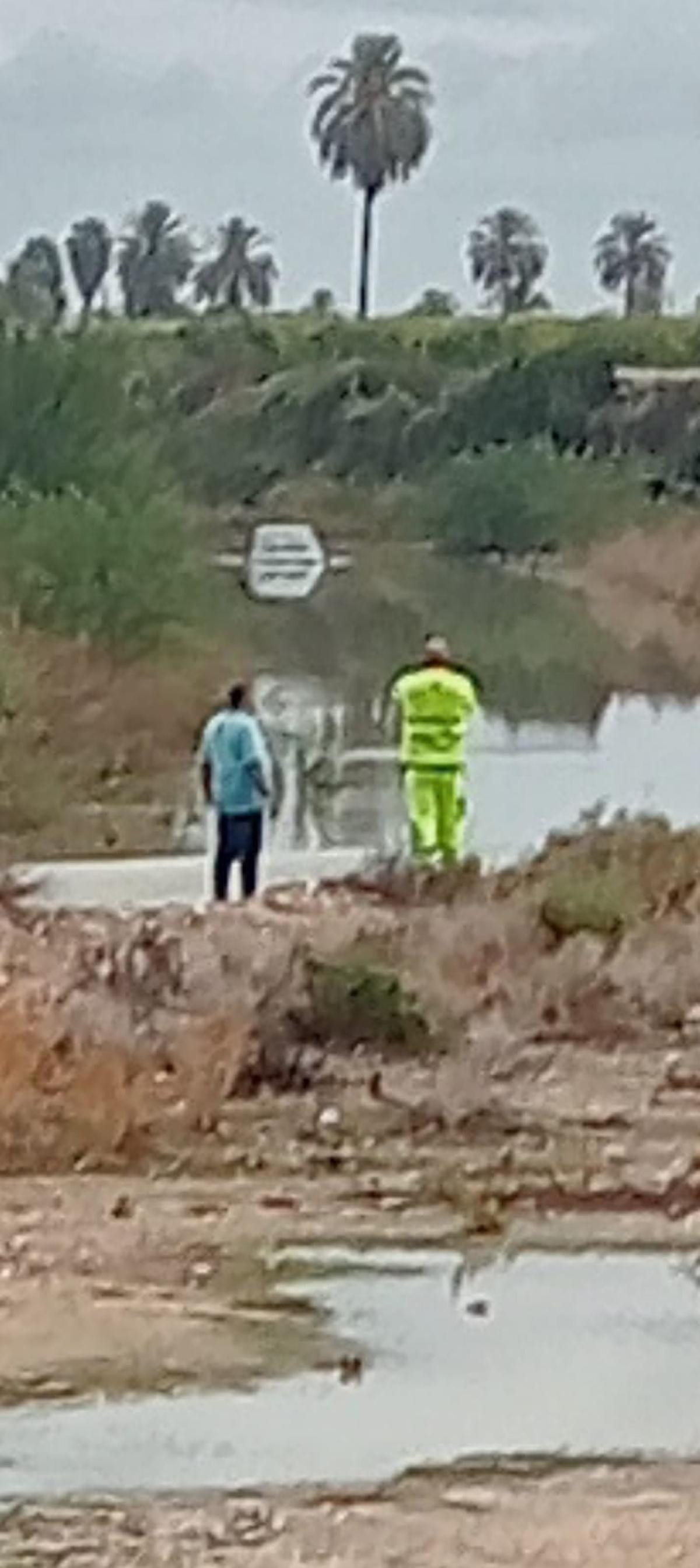 Accidentado y un técnico de la grúa observan el coche en medio del cauce del río Vinalopó en el campo de Elche