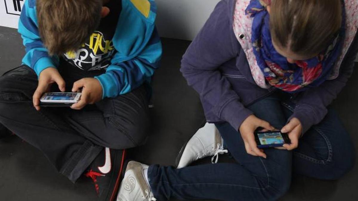 Un niño y una niña trastean con su móvil.