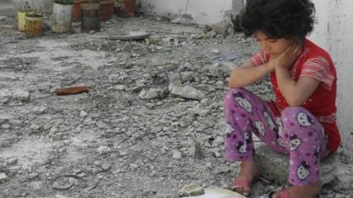 La pequeña Amira sentada en unas ruinas en su país natal, Siria.