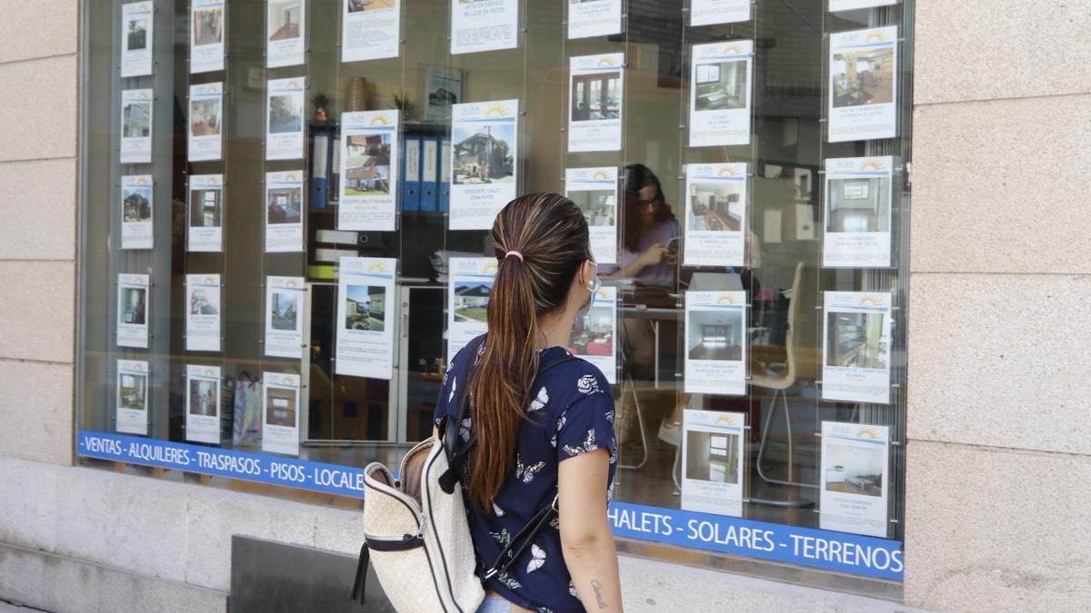 Una joven mira el escaparate de una inmobiliaria.