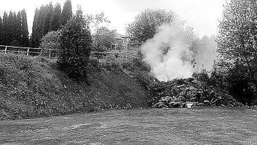 El montón de basura, en plena combustión, junto al vallado de la pista polideportiva de Candás.