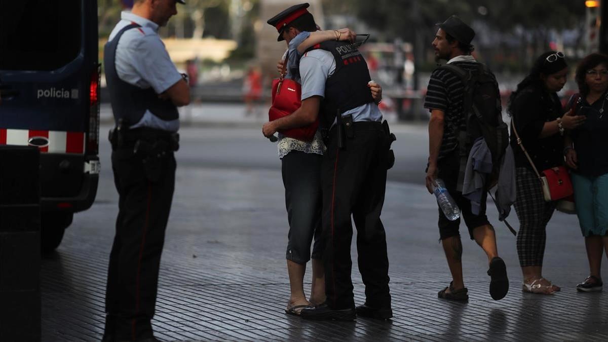 Una mujer abraza a un Mosso d'Esquadra tras visitar el memorial a las víctimas del atentado de Las Ramblas