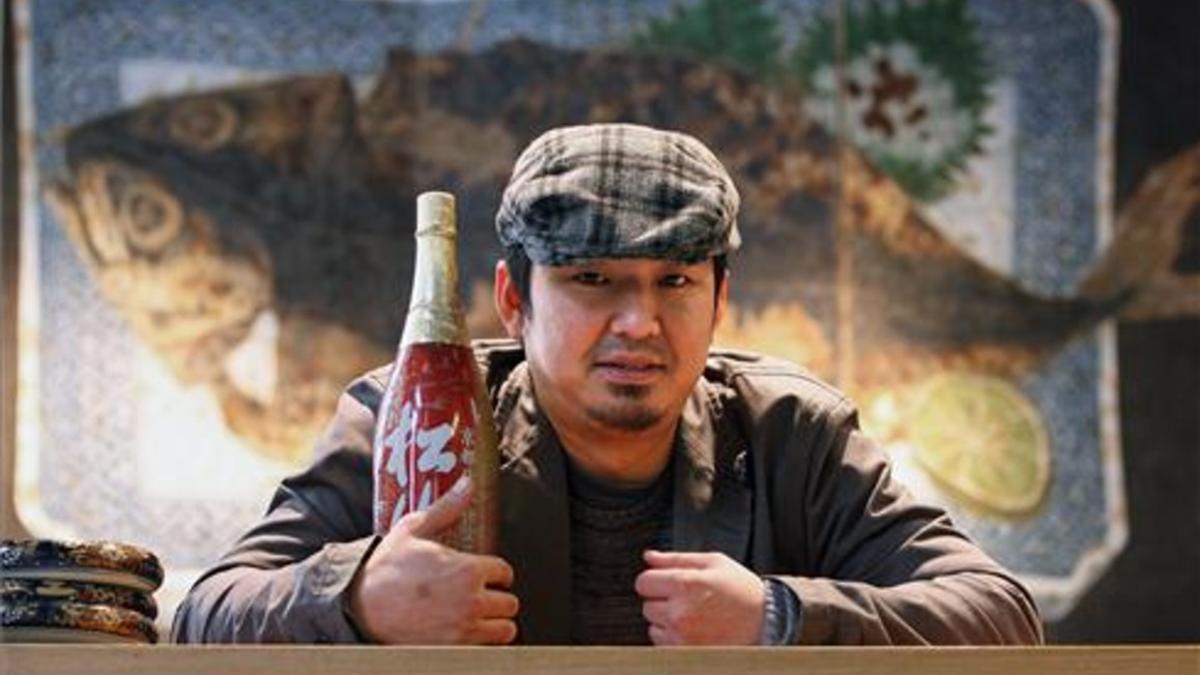 Kenji Ueno, con una botella de sake frente al cuadro de la caballa.