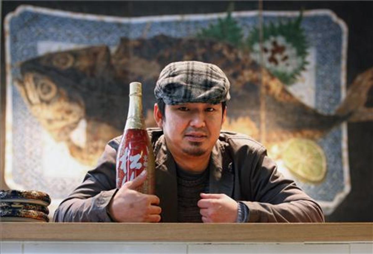 Kenji Ueno, con una botella de sake frente al cuadro de la caballa.