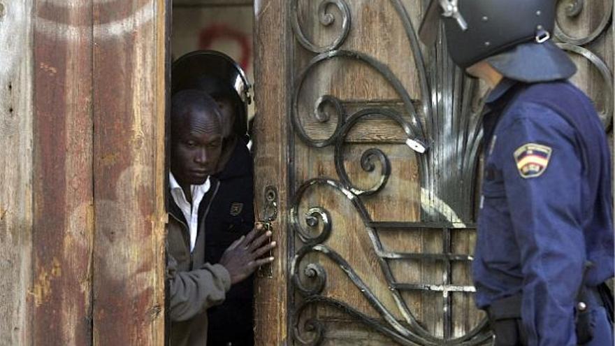 en la calle. Uno de los inmigrantes subsaharianos que ocupaba la fábrica de Bombas Gens sale por la puerta principal del edificio escoltado por los agentes del Cuerpo Nacional de Policía.