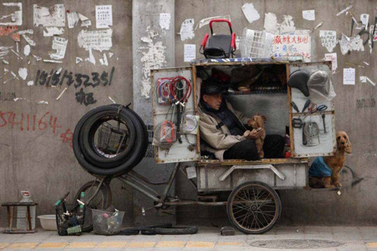 Un reparador de bicicletes acaricia el seu gos mentre espera clients en un carrer de Pequín.