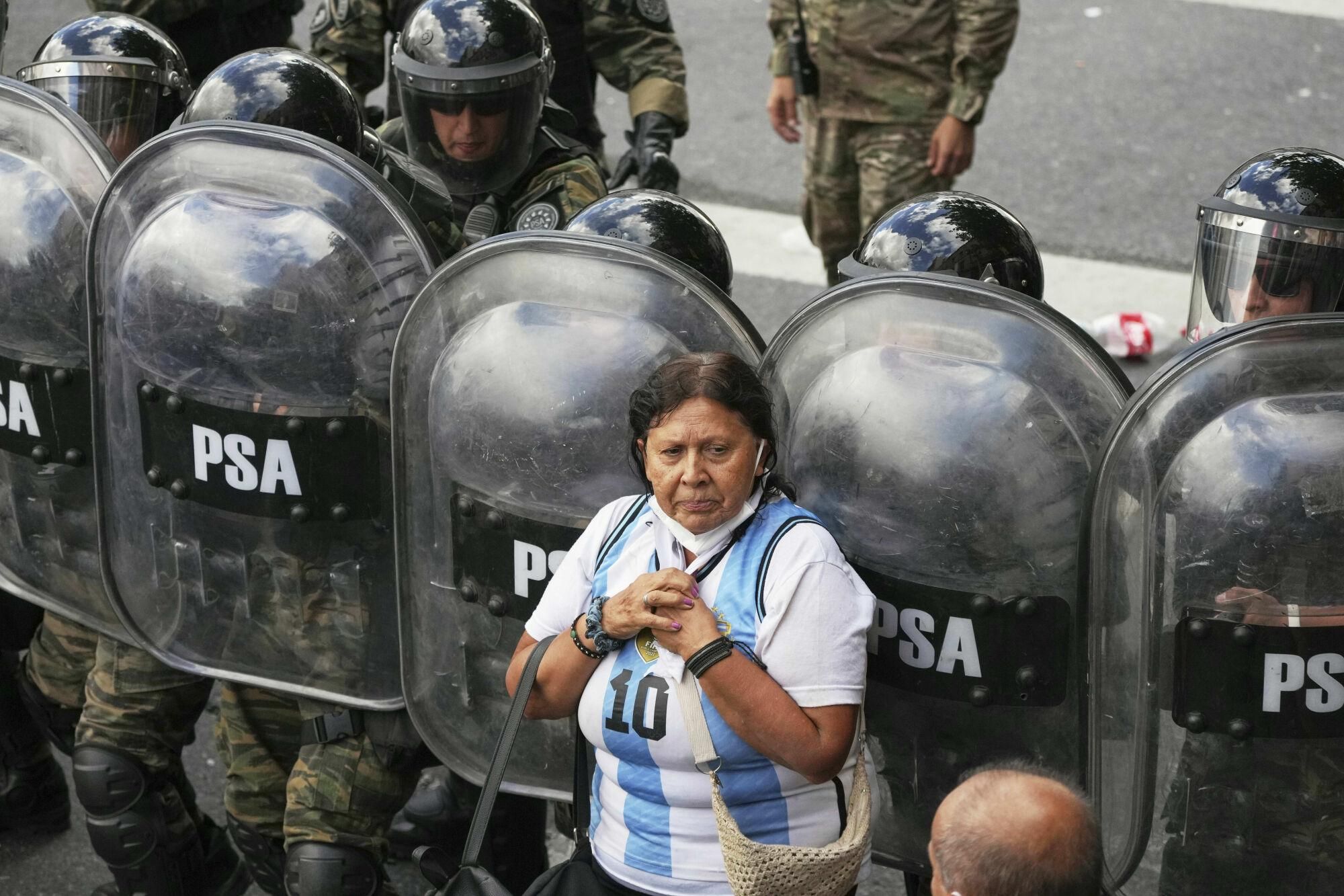 A woman stands in front of riot police during a protest by soccer fans and retirees demanding higher pensions and opposing austerity measures implemented by Javier Milei's government in Buenos Aires, Argentina, Wednesday, March 12, 2025. (AP Photo/Natacha Pisarenko). EDITORIAL USE ONLY/ONLY ITALY AND SPAIN