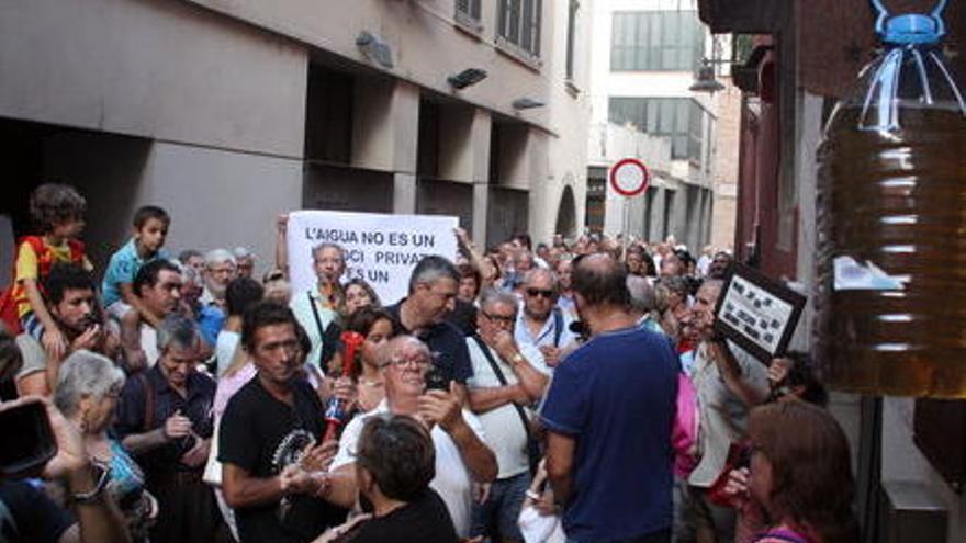 En primer terme, una ampolla omplerta amb aigua bruta que surt de l&#039;aixeta i, darrere, els veïns manifestant-se