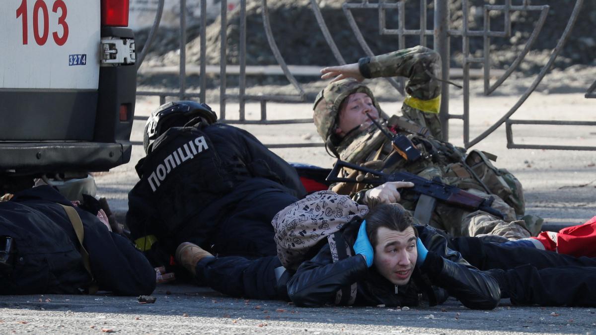 Unas personas se ponen a cubierto mientras suena una sirena antiaérea, cerca de un edificio dañado por los bombardeos en Kiev.