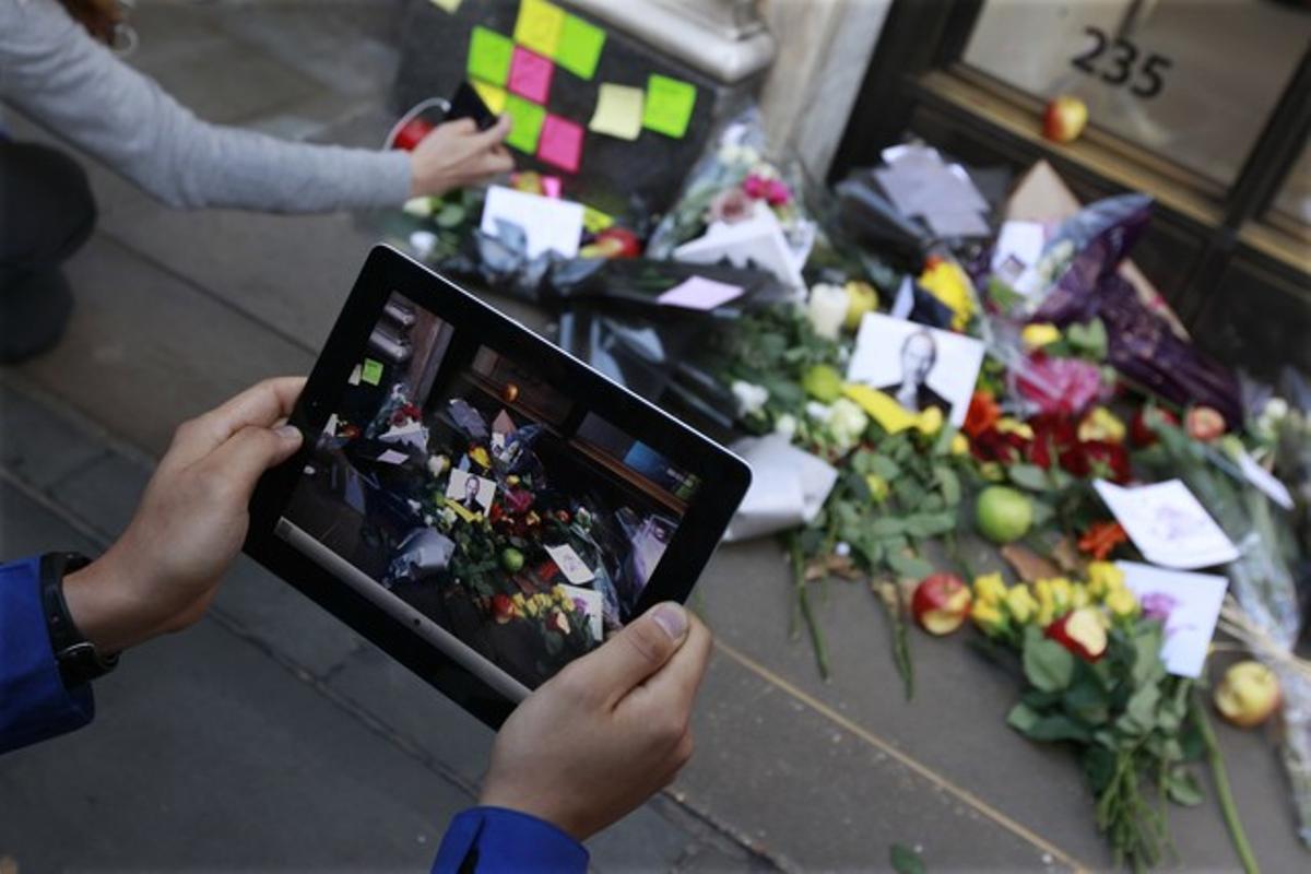 Un home fotografia amb el seu iPad les flors dipositades davant la façana de l’Apple Store de Londres(Regne Unit).