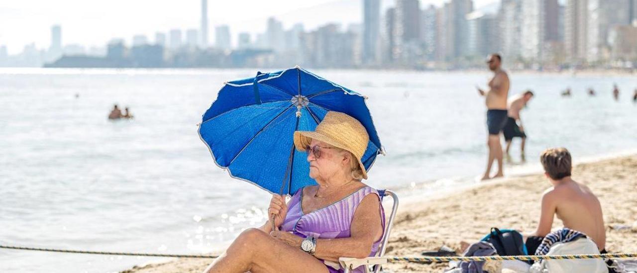 Una señora se protege del sol con una sombrilla en la playa de Levante de Benidorm