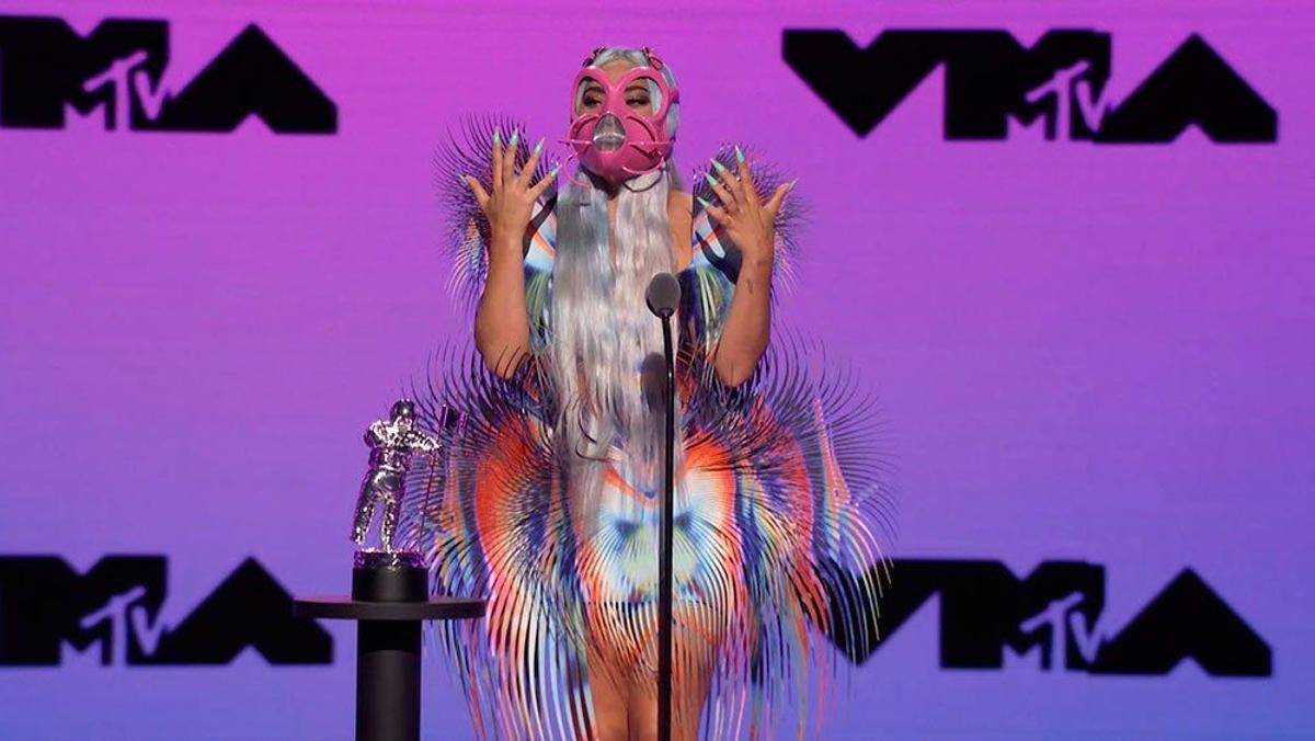 Lady Gaga con vestido tornasolado y plumas y mascarilla rosa