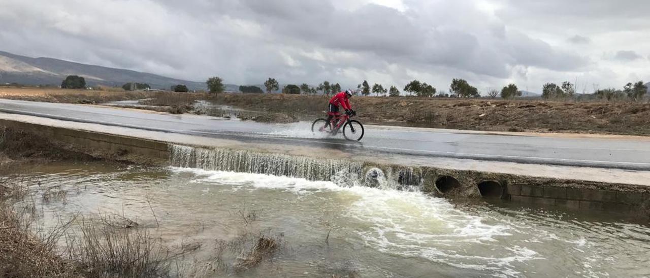 Un ciclista cruzando la carretera de Biar-Camp de Mirra inundada por las aguas del río Vinalopó.