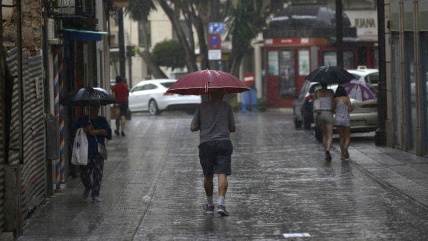 Varios vecinos caminan por una calle de Murcia mientras llueve.
