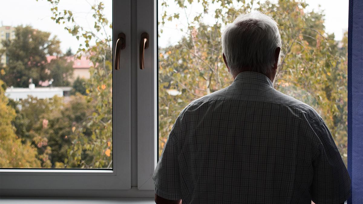 Una persona mayor mira por una ventana, en soledad.