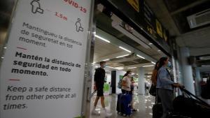 Pasajeros a su llegada al aeropuerto de Palma de Mallorca pasan frente a un cartel alusivo al coronavirus.