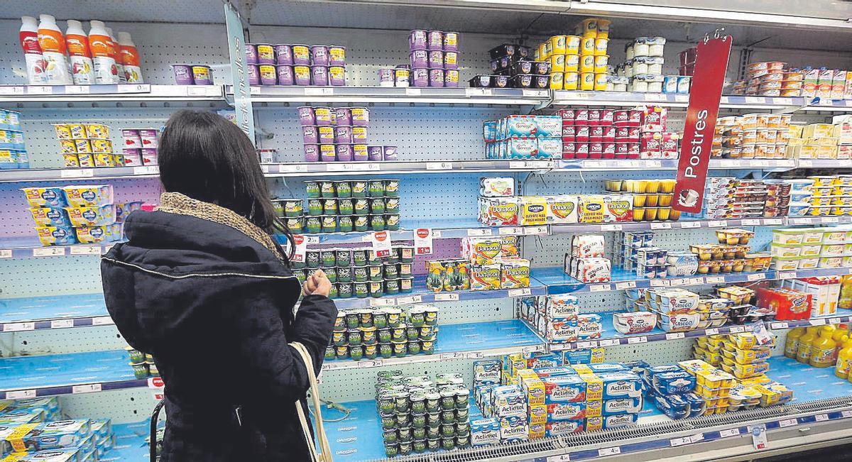 Una clienta de un supermercado observa una estantería con productos lácteos