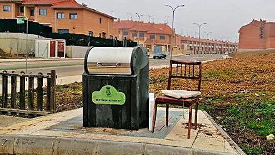 Una silla abandonada junto a un contenedor soterrado.