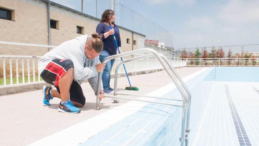 Lionel Rodríguez, anclando una escalera, y Cristina Palacio, con una escoba, ante la piscina vacía.