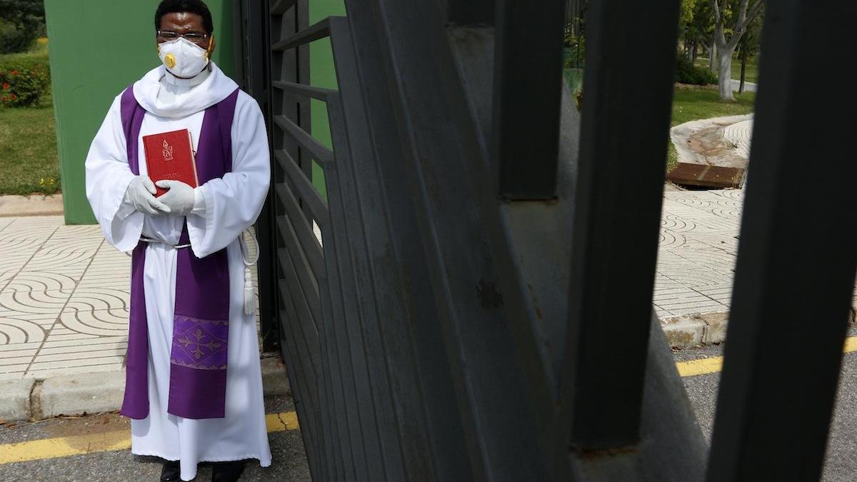 El sacerdote Manuel Esono, protegido con mascarilla y guantes para dar un responso.