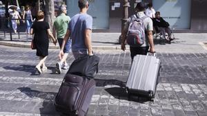 Dos turistas, con maletas, cruzan un paso de peatones.