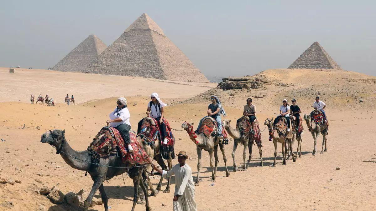 Turistas montan a camello por los alrededores de las pirámides de Guiza, en Egipto.