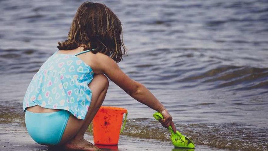 Una niña, con un cubo y una pala a la orilla del mar.