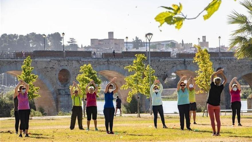 Varias personas mayores hacen deporte en el parque del río.