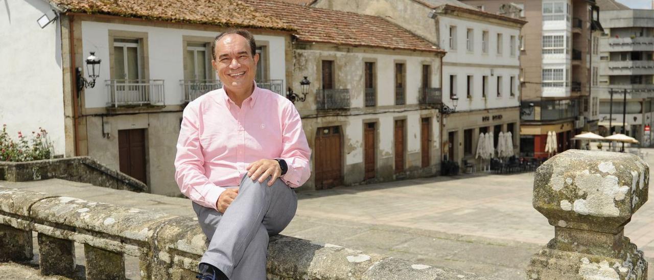 Crespo, ayer, con las piernas cruzadas, en la balaustrada del recinto de la iglesia, con las dos casas (al fondo) que comprará el Concello para hacer la Gran Praza.