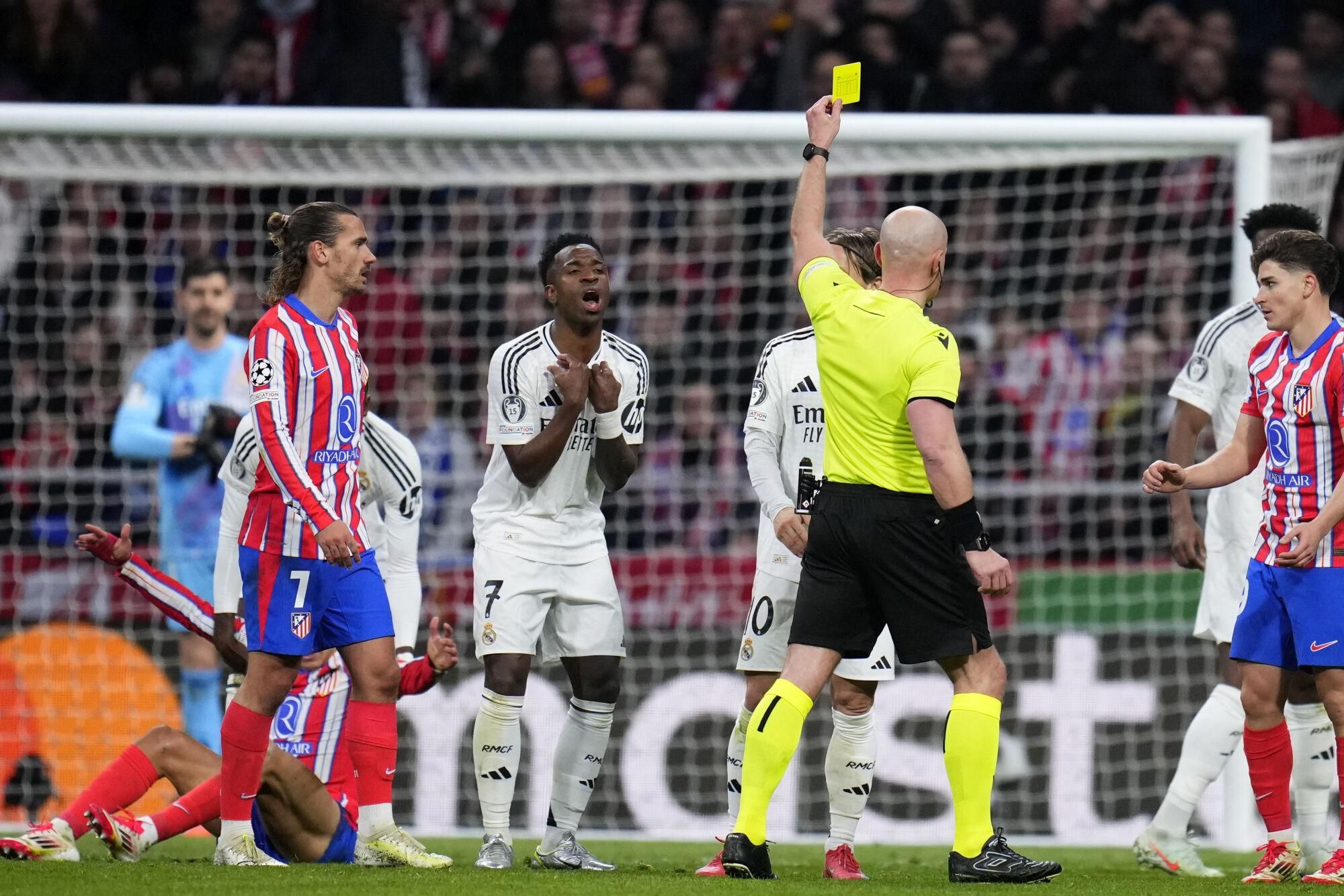Referee Szymon Marciniak shows a yellow card to Real Madrid's Vinicius Junior during the Champions League round of 16, second leg, soccer match between Atletico Madrid and Real Madrid at the Metropolitano stadium in Madrid, Spain, Wednesday, March 12, 2025. (AP Photo/Manu Fernandez). EDITORIAL USE ONLY/ONLY ITALY AND SPAIN
