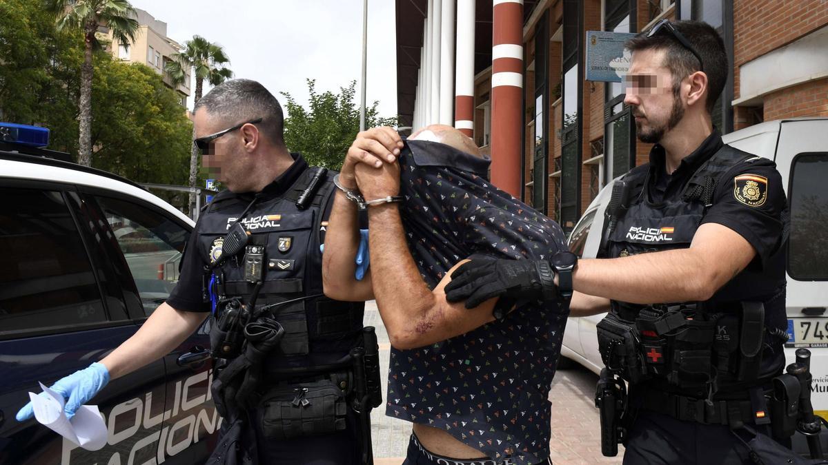 Uno de los detenidos trata de cubrir su rostro tras ser sacado del centro de salud del Infante, en Murcia, donde le curaron.