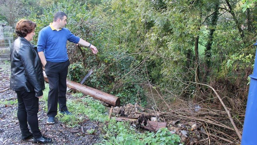 Toni Benítez, junto a Pilar Santianes, muestra las ramas y la basura acumuladas en el cauce del río Noreña.