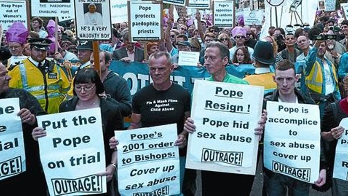 POSICIONES ENFRENTADAS El Papa recibe un bebé, arriba, al llegar ayer al acto de Hyde Park, en Londres. A la derecha, la marcha celebrada cerca del parque en la que se le acusa de encubrir los abusos. A la izquierda, un manifestante vestido de carden