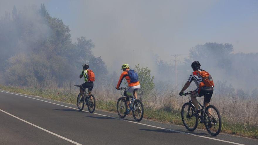 Varios ciclistas circulan por la zona donde se ha declarado el incendio.